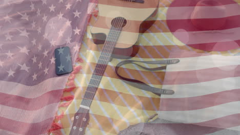 animation of american flag and light spots over guitar, smartphone and bag on beach towels in sun