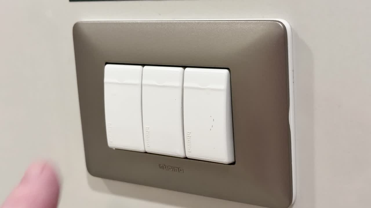 Person presses and switches off a triple light switch in a well-lit indoor environment
