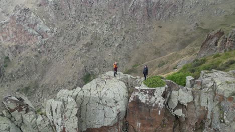 Aerial-orbits-man-and-woman-on-narrow-rock-fin-ridge-high-above-valley