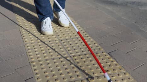 legs of blind person searching special tactile tiles using cane. blind man walking with a cane in the street