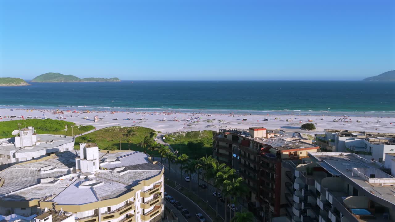 Vista aérea deslumbrante da Praia do Forte em Cabo Frio, Brasil. A cidade litorânea se encontra com uma enorme praia de areia branca repleta de turistas desfrutando do oceano azul profundo