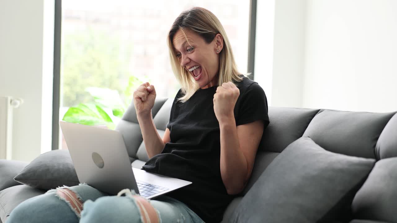 Excited woman celebrates success while using a laptop on a couch