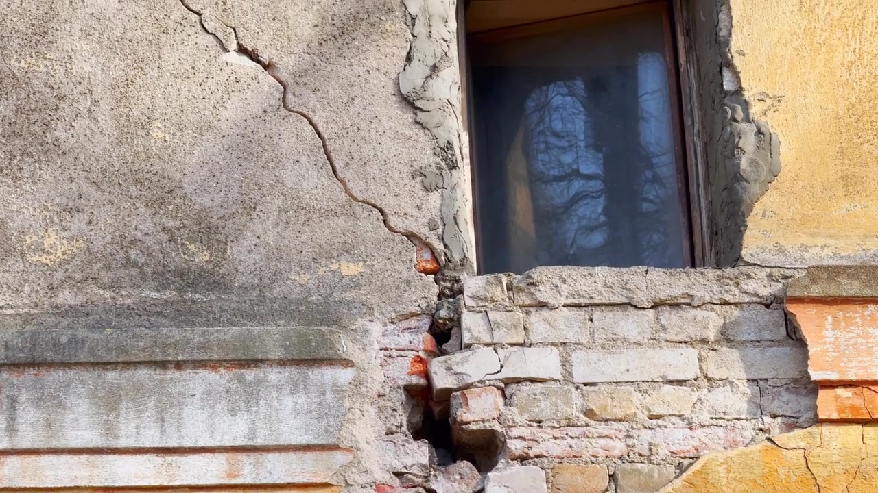 Primo piano di un vecchio muro di edificio danneggiato con mattoni a vista, intonaco screpolato, facciata scrostata e muratura deteriorata dalle intemperie sotto la luce solare intensa.