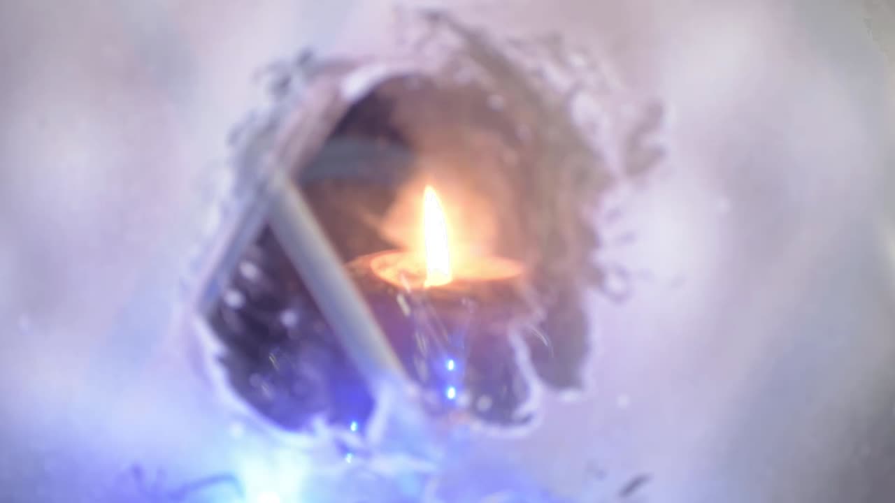Lit candle flame through snow window with blue Christmas lights