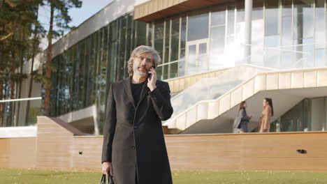 mature businessman talking on smartphone outside modern office building