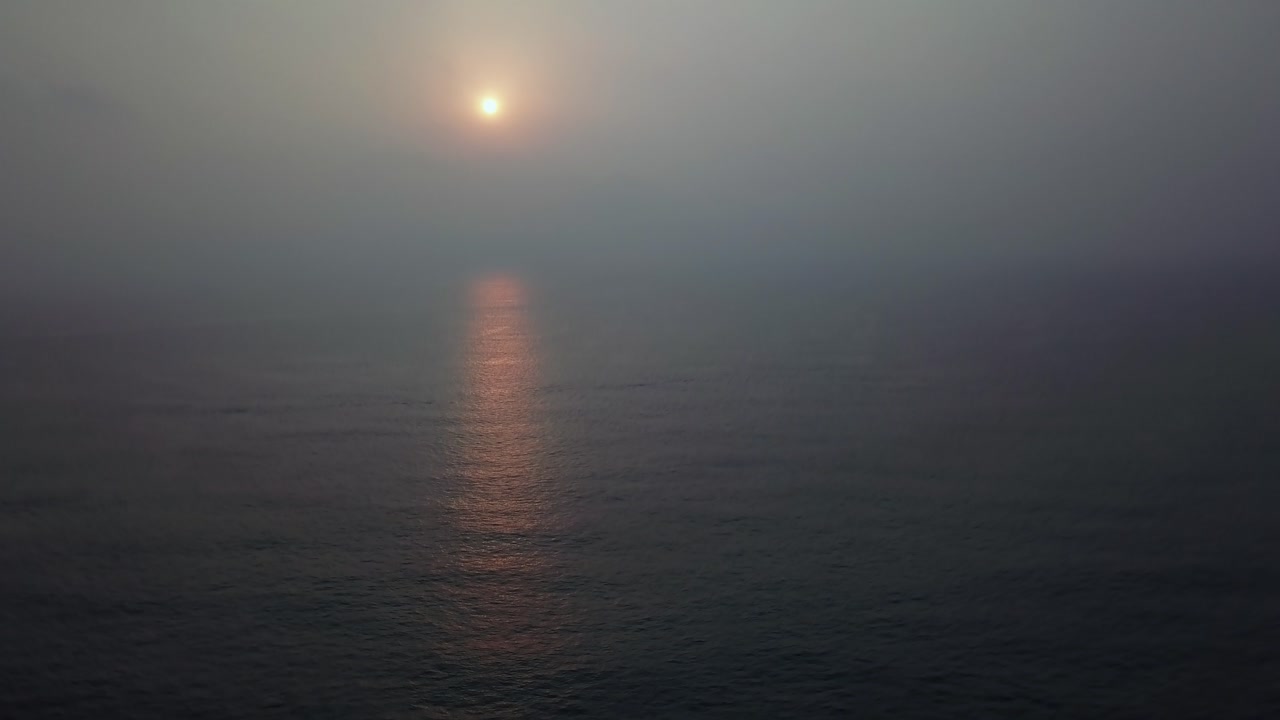 Sunset glowing through hazy atmosphere over the Arabian Sea at Candolim Beach, Goa, India. Golden light reflects on calm dark ocean water creating a luminous pathway during twilight hour.