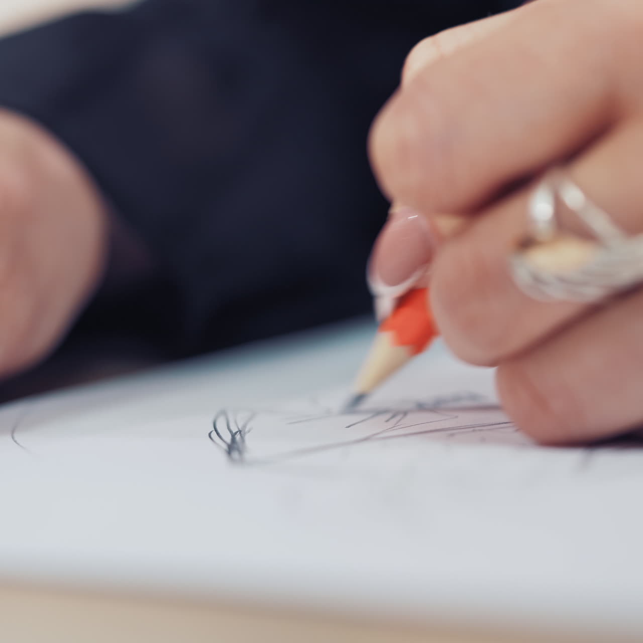 Woman's hand with a beautiful ring of a designer is drawing sketch of dress in atelier. Female tailor draws with a sharp pencil on the table. Close-up