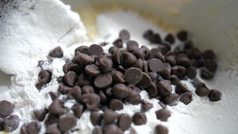 close up of chocolate chips being added to cookie dough cake mix with flour butter and sugar