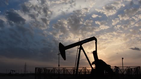 silhouette of crude oil pump standing still in the oilfield at cloudy sunset