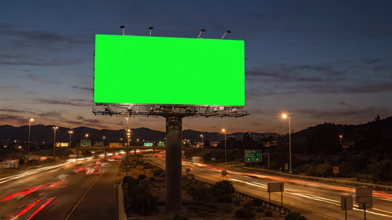 Et iøjnefaldende grønt billboard, der viser en ren reklameflade midt på en naturskøn motorvej i skumringen og om natten, og som indfanger overgangen fra dag til nat.