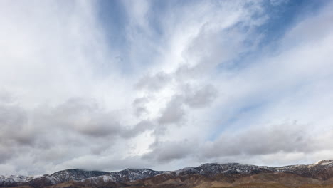 dos capas de nubes moviéndose en direcciones separadas sobre las montañas tehachapi cubiertas de nieve - lapso de tiempo estático