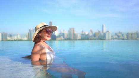 young rich asian woman relaxing in a luxurious infinity pool with an incredible view of bangkok cityscape in the background, she is leaning on her elbows, side view slow-motion