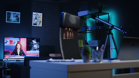 dimly lit apartment with office desk in front of smart tv displaying news program