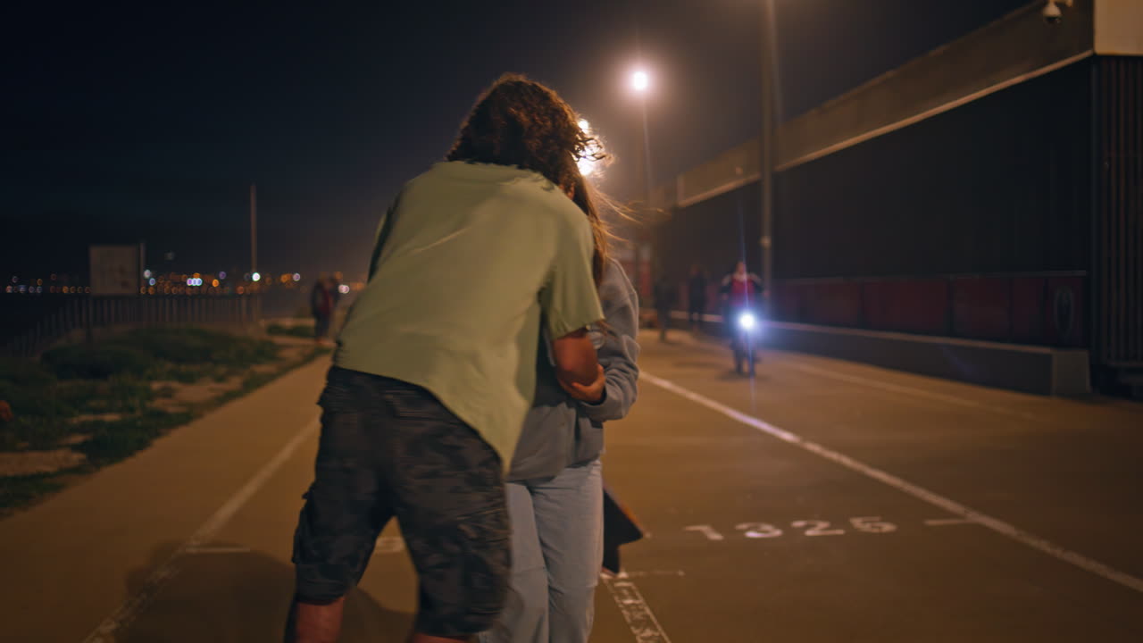 романтические конькобежцы целуются ночью асфальтная дорога. спортивная пара наслаждается активным свиданием