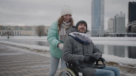 happy caucasian woman taking her disabled friend in wheelchair for a walk in the city. they talking together and looking at something interesting in the sky.