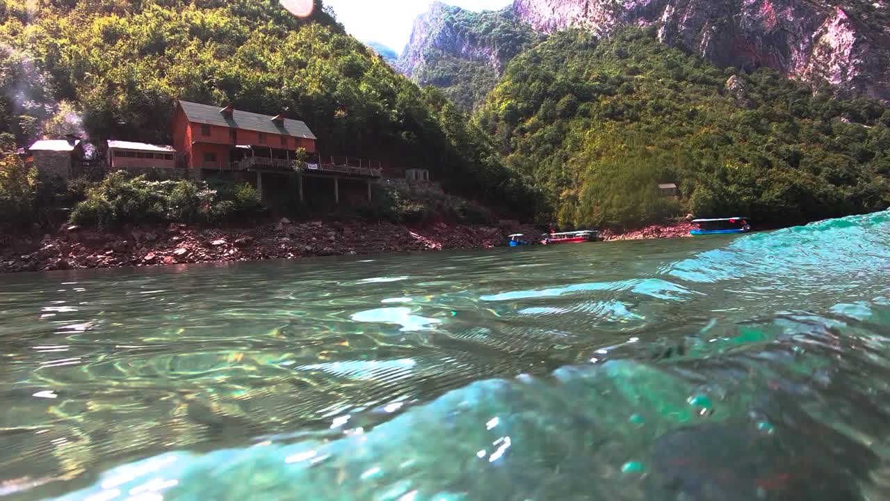 Clear crystal water of river streaming alongside Alps mountain slope with vacations resort surrounded by green vegetation