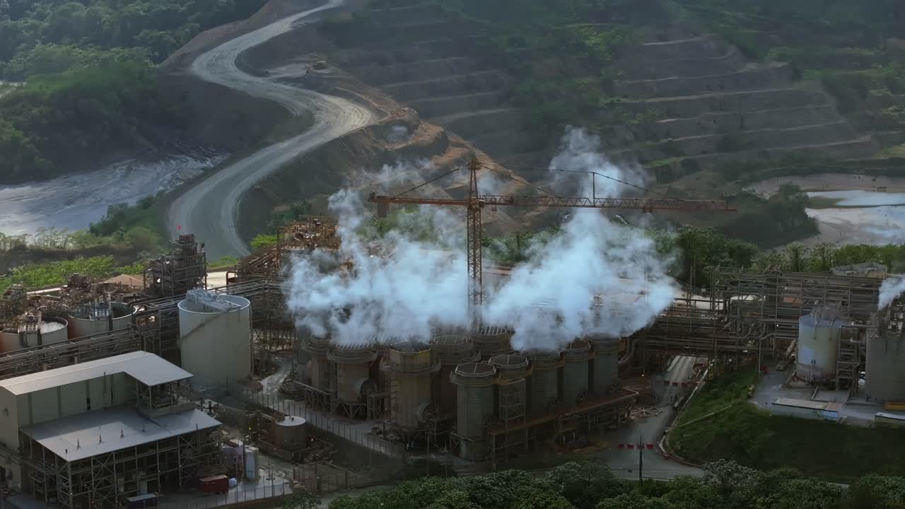 Static aerial shot of industrial plant with smoke emissions, terraced hills, Cotuí, Dominican Republic.