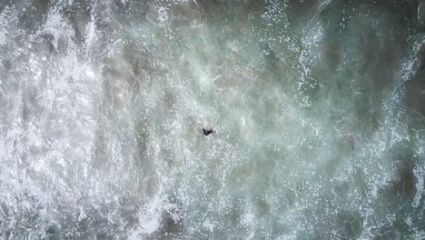 vista aérea de arriba hacia abajo de un surfista pisando el agua mientras se acercan grandes olas