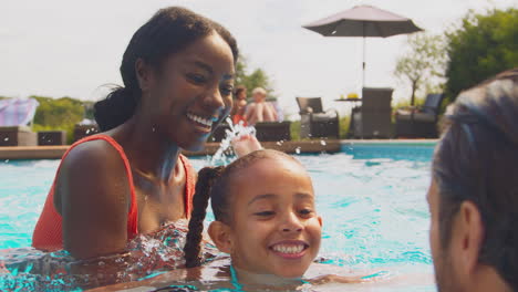 family having fun splashing with daughter in pool on summer holiday