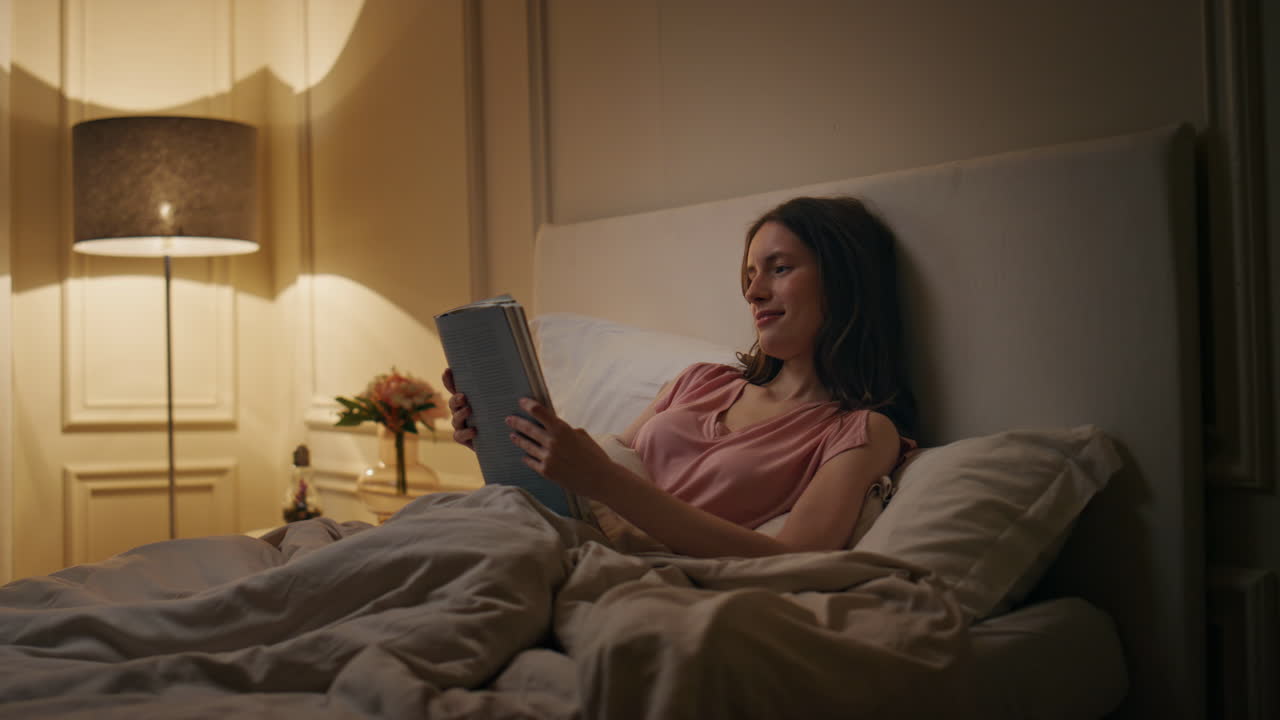 Peaceful woman reading book in evening home. Smiling reader enjoying novel rest