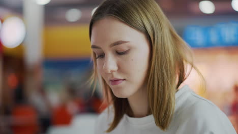 primer plano de una mujer enfocada y profundamente pensada mientras está sentada en un entorno comercial, el fondo colorido borroso presenta iluminación suave y espacios comerciales