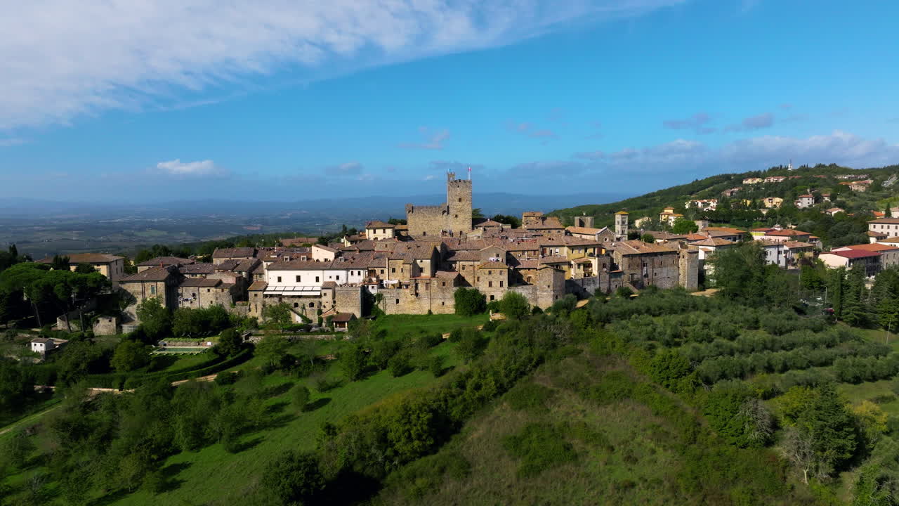 Rocca di Castellina, Castellina in Chianti, Toscana, Italia - Una città medievale in cima a una collina domina la campagna verde e ondulata sotto un cielo azzurro e limpido - Ripresa aerea orbitale con drone