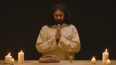 fotografía de estudio de un hombre vestido con túnicas, cabello largo y barba que representa la figura de jesucristo bendiciendo el pan y el vino 2