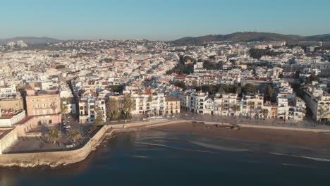 El-Dron-Vuela-Lejos-De-La-Turística-Ciudad-Costera-Iluminada-Por-El-Cálido-Sol-De-La-Mañana-Mientras-Las-Suaves-Olas-Del-Mar-Se-Deslizan-Silenciosamente-Hacia-La-Orilla