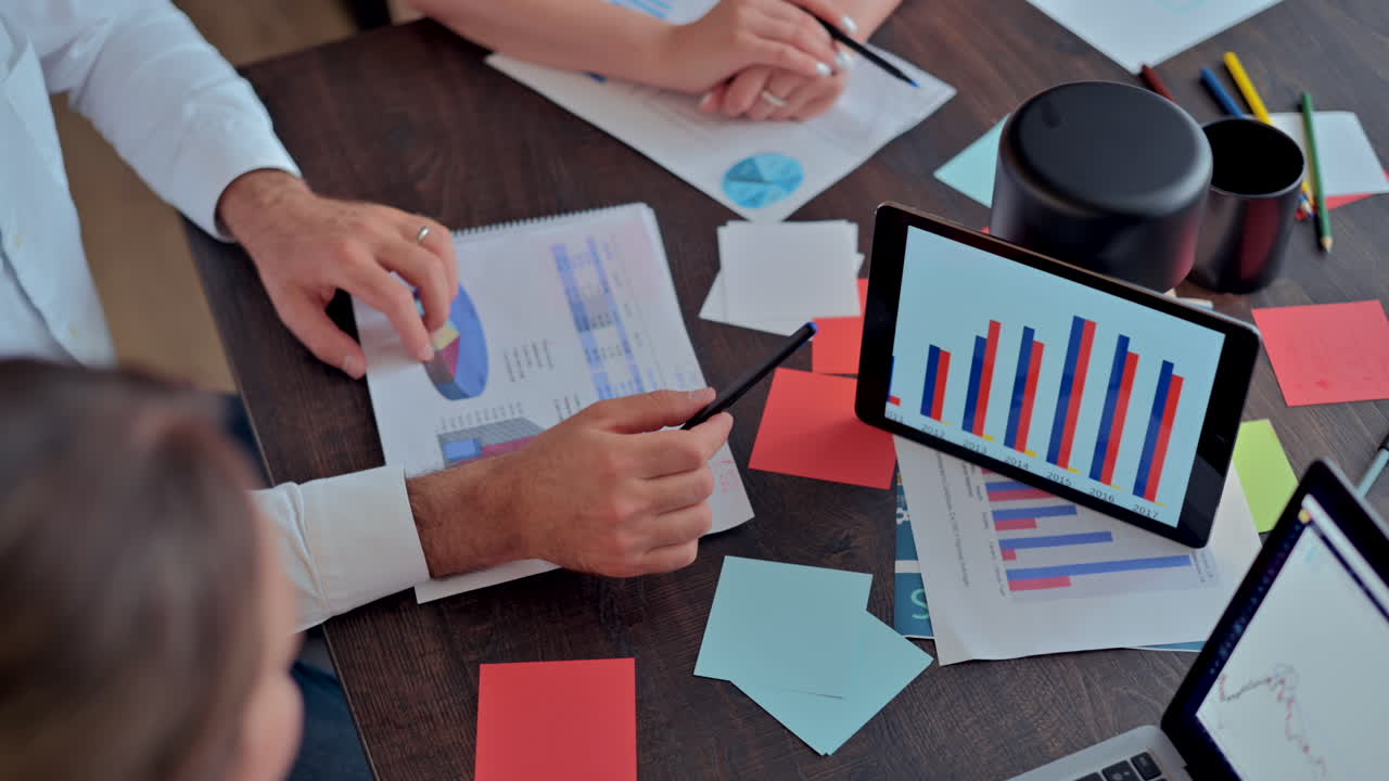 Three coworkers analysing a graph on a tablet at a desk, in an office