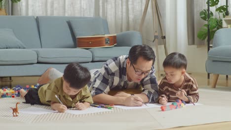 아시안 아버지와 아들의 몸이 가득 차 있고, 플라스틱 장난감 벽돌이 있는 방에서 바닥에 누워서 집에서 함께 그림을 그리고, 이야기하고, 놀고 있다.