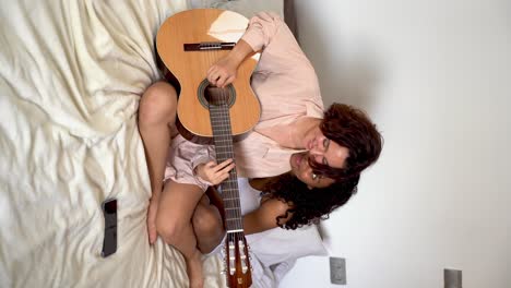 joven europea concentrada tocando la guitarra mientras su novia afroamericana se apoya la cabeza sobre el hombro y disfruta de la música