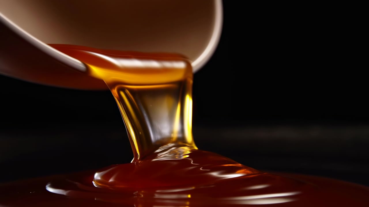 Liquido che si versa da una tazza, azione di versamento, su sfondo scuro, con tazza, liquido, vetro e texture di sostanza liquida, da una prospettiva ravvicinata, con accenti marroni e arancioni.