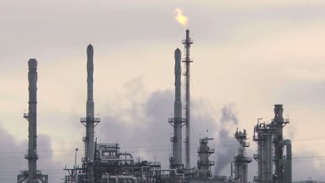 a dramatic image of an oil refinery silhouetted against the evening sky, with smoke billowing from the stacks.