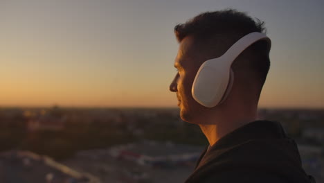 close-up of a man in headphones looking at the city from the height of a skyscraper at sunset. relax while listening to music. enjoy a beautiful view of the city at sunset from the roof with headphones.