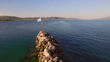 Aerial:-Small-fishing-town-with-Greek-flag-on-Samos-island,-Greece