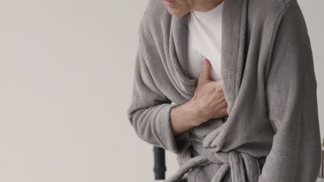 close up of man wearing pajamas and robe having chest pain at home