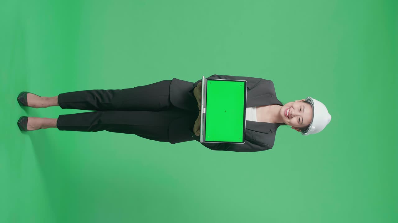 Full Body Of Smiling Asian Female Engineer With Safety Helmet Showing Green Screen Laptop In The Green Screen Studio