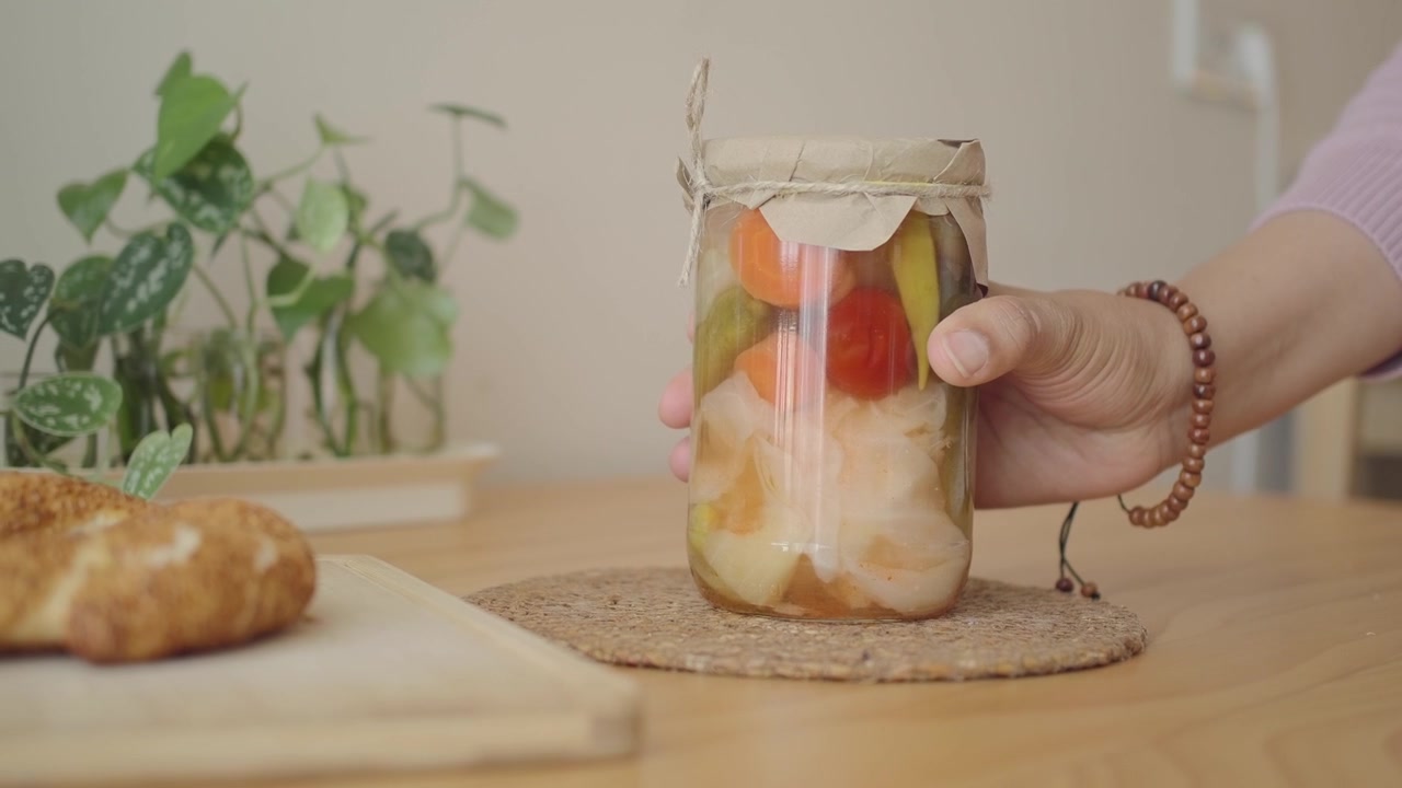 Mão Pegando um Pote de Vegetais em Conserva de uma Mesa de Madeira