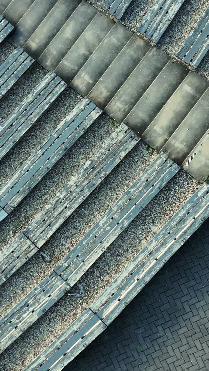 Salueskalns Weathered wooden benches lining cobblestone pavement at historic open air theater, revealing architectural heritage of Talsi, Latvia, top down vertical drone close up