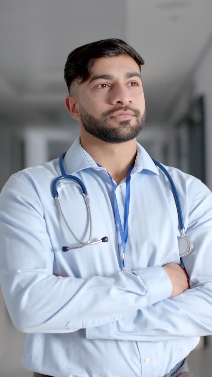 Vertical video of portrait of happy biracial male doctor in hospital corridor, slow motion
