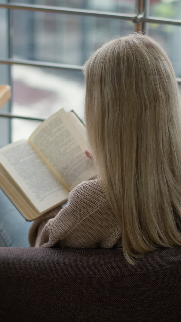 vista posterior de una estudiante preparándose para un examen, enfocada mientras pasa a una nueva página de su libro de texto mientras está sentada en una mesa en un área de estudio con una taza de café y un teléfono a su lado