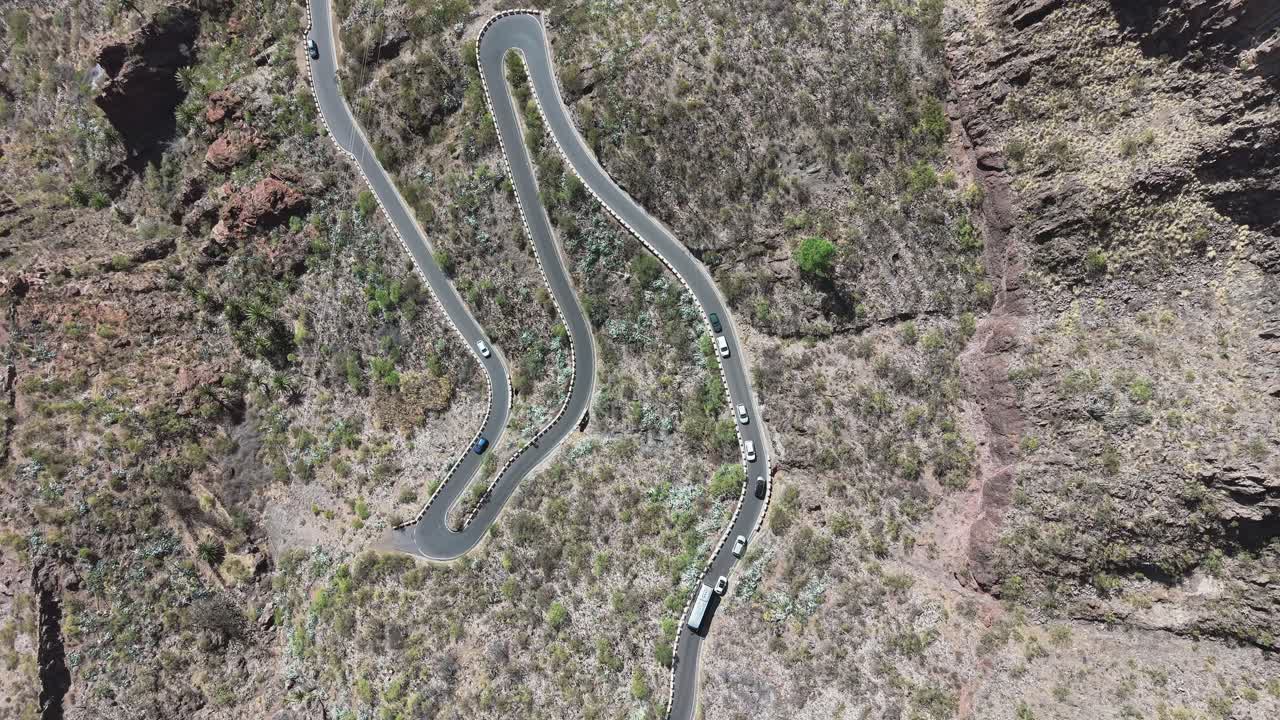 Top-down drone fly over winding mountain road with cars navigating safely sharp bends in dry rocky terrain, Tenerife, Canary Islands, Spain