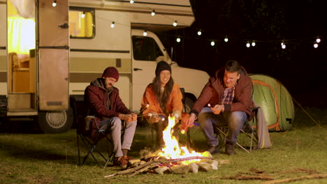 grupo de amigos felices alrededor de un fuego de campamento ardiente