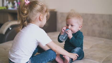 la niña ayuda al hermano pequeño a beber agua de la botella en la cama