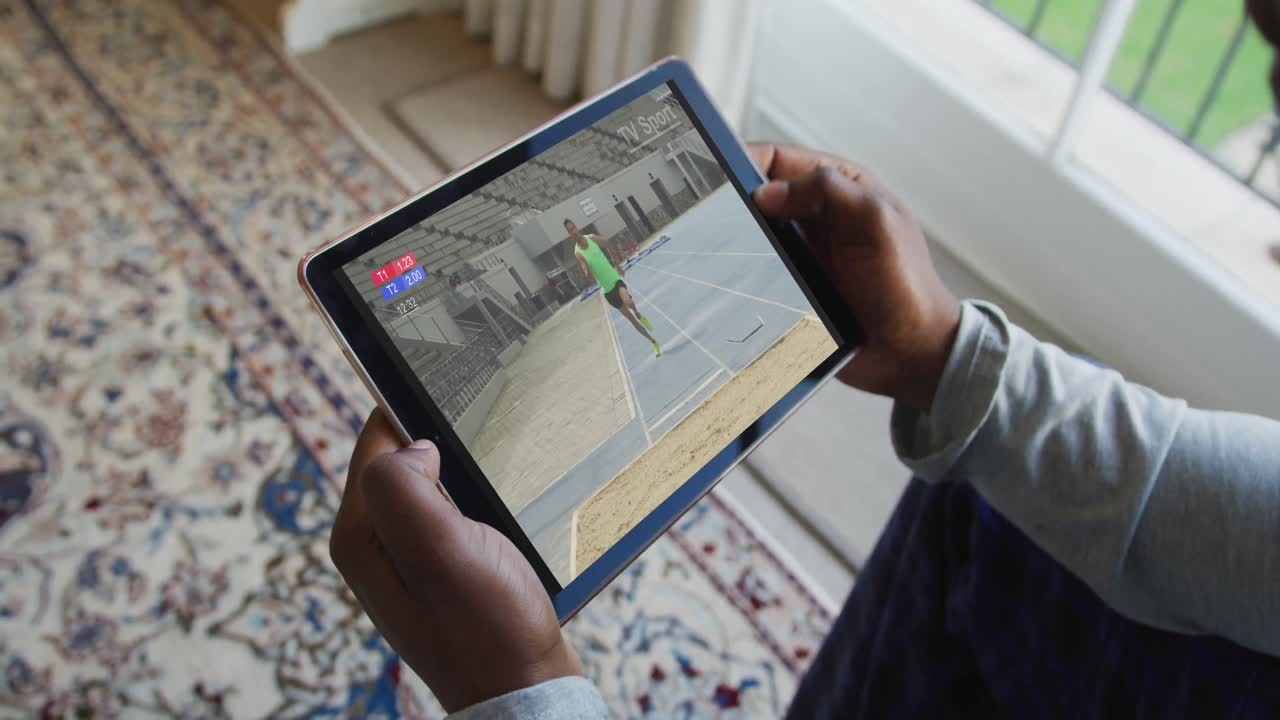 compuesto de un hombre sentado en casa, viendo el evento de salto de longitud de atletismo en la tableta