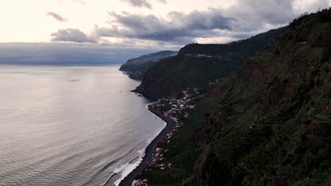 sunset aerial along rugged madeira coastline, small coastal village