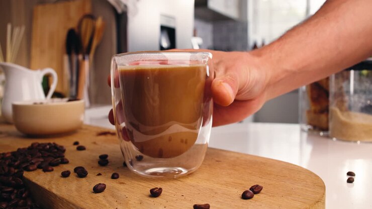 Mano che prende un bicchiere di latte macchiato da una tavola di legno