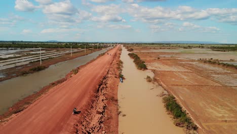 Red-or-orange-dusty-road-in-Cambodia,-aerial-drone-view-of-typical-countryside-highway