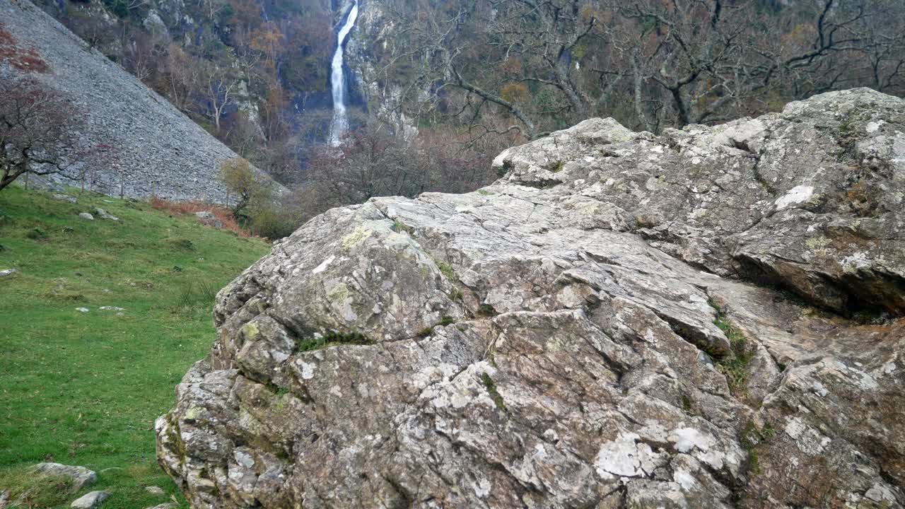 sendero natural de otoño que conduce a una cascada detrás de una gran roca rodante a la izquierda