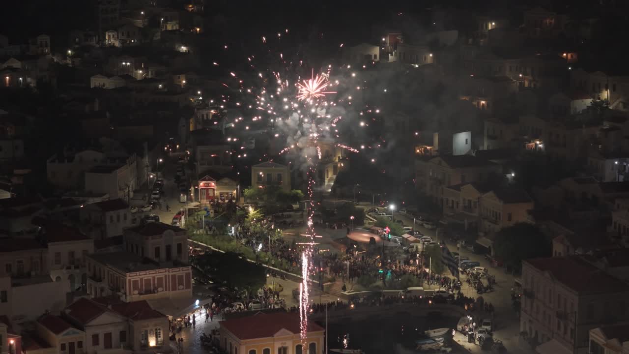 Cinematic shots of brilliant fireworks bursting over Symi harbor with lights reflecting on boats and historic buildings. Filmed with 3x telephoto D-Log M